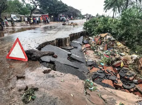 STRINGER/AFP Residents stand next to a road partially destroyed by floods after heavy downpours in Pemba