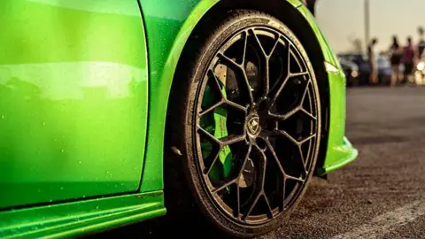 Getty Images A stock image of a car meet, showing the front bumper of a bright green sports car in a car park, with attendees in the background blurred out.