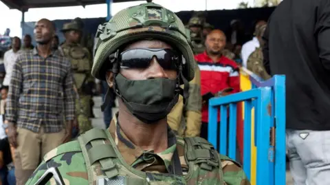 Reuters An M23 rebel with a face mask and dark glasses stands guard