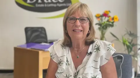 Zoie O'Brien/BBC Linda Druce from Druce Estate & Letting Agents sitting in her office smiling into the camera 