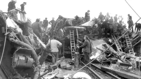 Walter Bloxham/Warwickshire Police/Nuneaton Memories People stand around the wreckage and on top of it. Ladders can be seen leaning against it while pipes and bricks are strewn around.