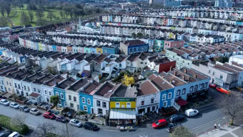 Rows of colourful houses in Totterdown in south Bristol from a bird's eye view, on a clear day. In the background a park is visible.
