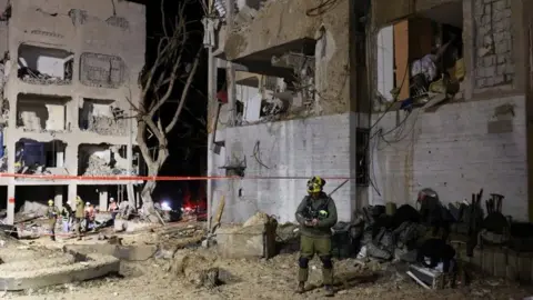 Reuters Devastated apartment blocks at night in Arad, with emergency worker in foreground
