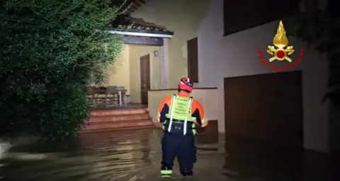 Vigili del Fuoco A firefighter wading into a house amid floodwater