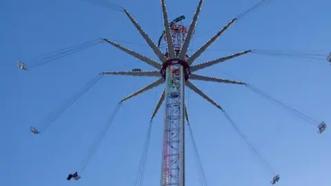 A view of the fairground ride - a tall central metal structure with swings flying around in a circle