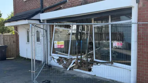 The front of the Lady and the Tramp Groomers in Cleadon, which has been smashed. The windows are hanging off and there is debris at the front. The area is surrounded by security fencing and there are signs warning of the danger.