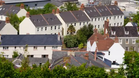 An image of houses in Guernsey taken from above, with grey roofs and white walls and trees peppered between them.