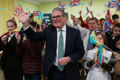 Carl Court/PA Media Prime Minister Keir Starmer waves with schoolchildren waving British and Ukraine flags in Kyiv 