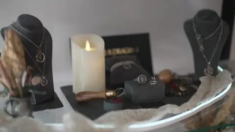 Una colección de joyas a medida de House of the Dragon reposa sobre una mesa que también tiene una vela blanca encendida.