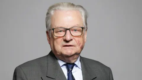 PA Media A man with grey hair, wearing glasses and a grey suit and blue tie