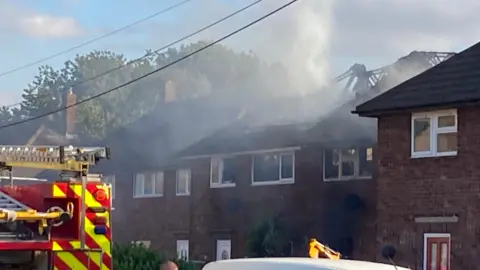 BBC The scene of a residential fire in Metheringham. There is a fire engine visible in the foreground, with smoke rising from the roofs of two properties, which appear to have collapsed.