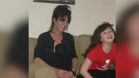 Supplied A woman and girl are sitting on a beige sofa looking at the camera. The woman has long dark hair tied in a ponytail. She is wearing a black top and has her hands clasped on her lap. The girl, who is aged about 10, is leaning forward and smiling at the camera. She has long dark hair and is wearing a red T-shirt.