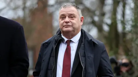 Reuters Mike Amesbury wearing a white shirt, red tie and dark overcoat