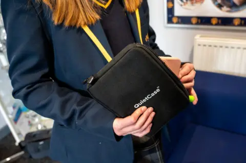 Northamptonshire police, fire and crime commissioner A girl in a navy school blazer holding a black pouch with a zip on the side. "Quiet Case" is written in white lettering on the side. 