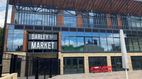 Bradford Council Entrance to a new market shows a stone building with black and grey windows and wood detailing