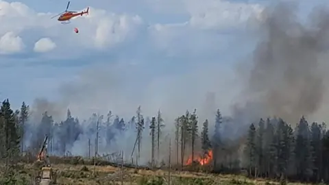 North Yorkshire Fire and Rescue Service Image shows a large moorland fire on Langdale Moor in North Yorkshire with a helicopter seen at the top of the image carrying a large water bowser