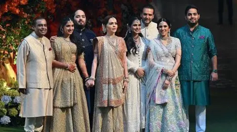 Getty Images Indian billionaire Mukesh Ambani (L) along with his wife Nita (4L) pose with their elder son Akash (R) his wife Shloka (2R), daughter Isha (4R) her husband Anand Piramal (3R) and younger son Anant (3L) his fiancée Radhika Merchant (2L) during Anant's engagement ceremony in Mumbai on January 19, 2023.