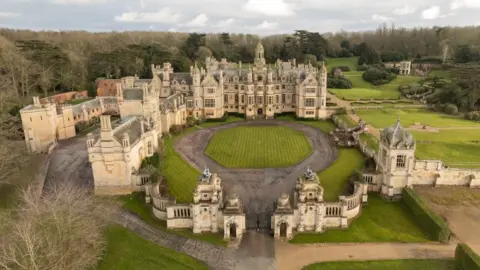 Harlaxton Manor An aerial view of Harlaxton Manor in Lincolnshire. The house is surrounded by a large wall featuring several towers. A circular lawn in situated in the centre of a courtyard in front of the main building. Landscaped gardens are on the right of the image.