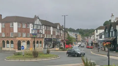A road with a roundabout in the middle. Shop line the road coming off it.