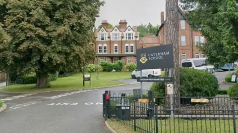 A private school is seen behind a fence and sign. 