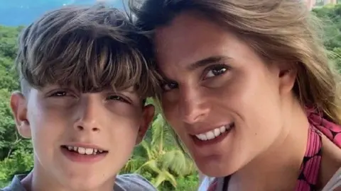 Ellen Roome A boy is pictured smiling standing next to his mum, who is also smiling at the camera.