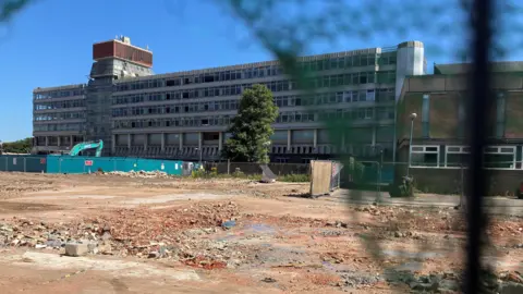 Owen Sennitt/BBC A large concrete and glass office block, Sovereign House was built in a brutalist architectural style. It can be seen from a distance across a demolition area, with security netting blurred in the foreground