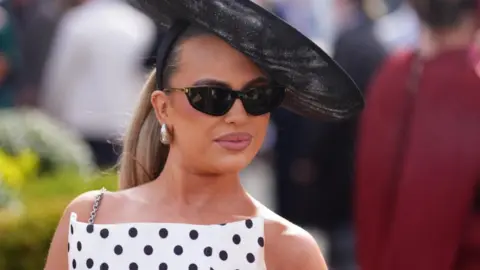 PA Media A woman in a white and black polka dot dress and black fascinator and sunglasses