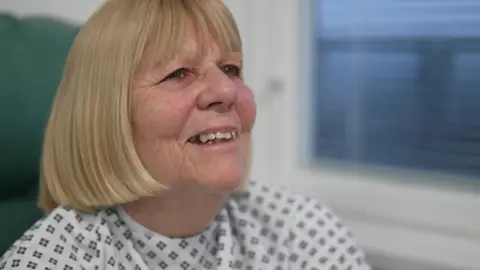 Margaret Georgian is chatting with a BBC reporter and a surgical patient is dressed in a gown