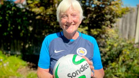 Sue Foulkes, football fan, in her Leicester City kit holding a signed football