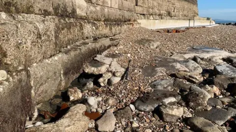 The sea wall of the cobb. There appears to be holes in the side of the wall with rocks and sand on the floor.