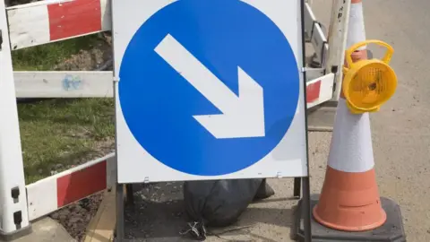 Getty Images A blue sign indicating road works is taking place. There is also a witch's hat next to the sign.