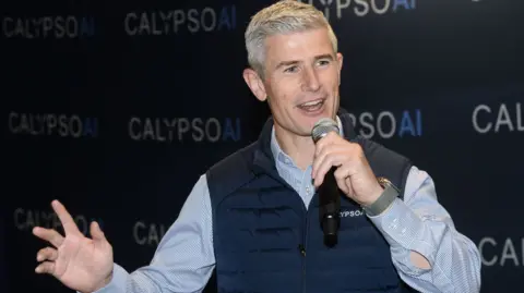 Calypsoai Donnchadh Casey, con una compañía de marcas de chalecos, habla en una conferencia.