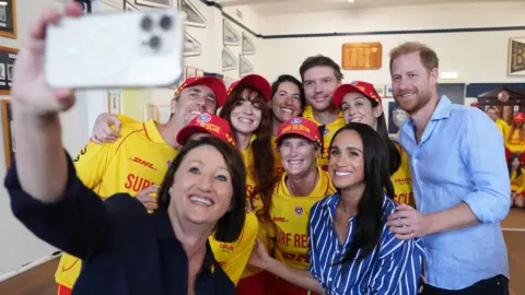 Getty Images The Duke and Duchess of Sussex pose for a selfie photo as they meet volunteer first responders from Bondi Surf Bathers' Life Saving Club