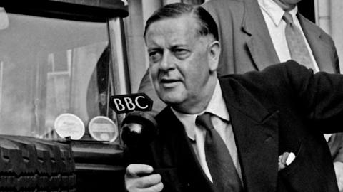 A black and white photograph of Robert Reid holding a BBC microphone.