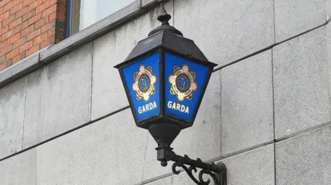 A Garda lamp. It is blue and black and attached to a wall.