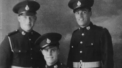 MOD Three men dressed in military uniform are smiling as they pose in formal black and white photograph.