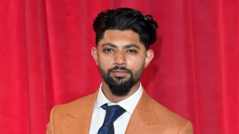 Qasim Akhtar in a suit standing in front of a red curtain