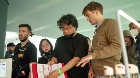 Alamy Bong Joon Ho and Robert Pattinson speak to one another as one of them holds a sheet of paper while they film Mickey 17.