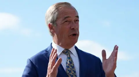 Nigel Farage standing outside, wearing a navy blue suit and a yellow and blue tie