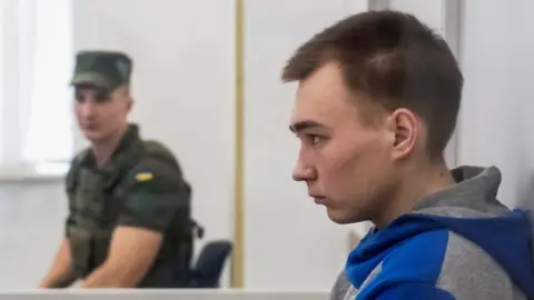 Reuters Vadym Shishimarin looks dead ahead, seen from the side, in a court, flanked by military guards