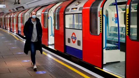 Magnum Photos A woman wearing PPE (personal protective equipment), including a face mask as a precautionary measure against COVID-19, walks along the platform alongside a London Underground Tube train in the morning rush hour, on May 11, 2020