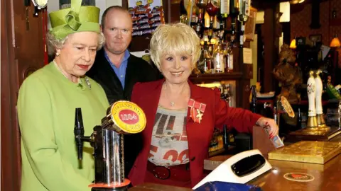 PA Media Queen Elizabeth II alongside Barbara Windsor and Steve McFadden in the Queen Vic pub in 2001