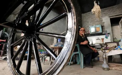 Reuters Egyptian craftsman Aly Gaber smokes shisha beside a horse-drawn carriage which he is working on, in his workshop in Alexandria, Egypt April 23, 2018