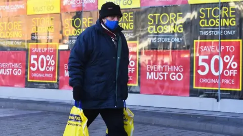 Getty Images Man walking past shop with 'closing down' signs