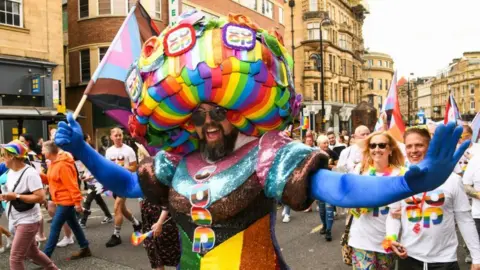 Haydn Brown/Northern Pride A bearded man wearing a rainbow dress parades through the city