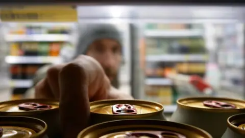 Getty Images Close-up of a man taking a beer from a supermarket fridge