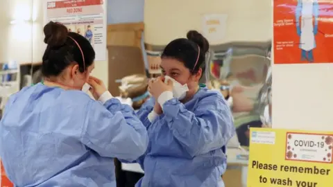 PA Media A healthcare worker placing a PPE mask on her face