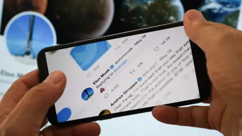 Getty Images Elon Musk's poop emoji reply to Parag Agrawal shown on a smartphone screen with Musk's Twitter page in background