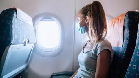 Getty Images A woman sits in an aeroplane wearing a mask