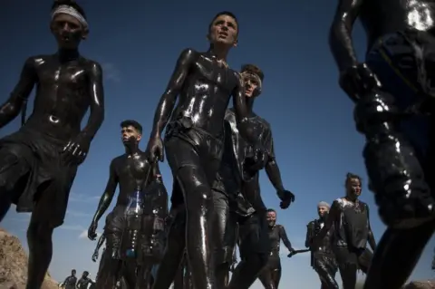 JORGE GUERRERO/AFP People covered in black grease walk together.
